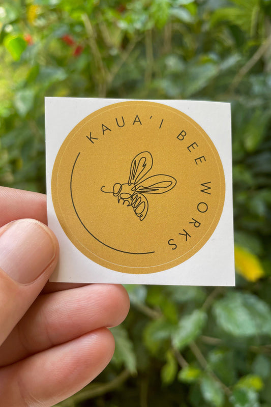 Kaua'i Bee Works 2" round sticker in front of green plants